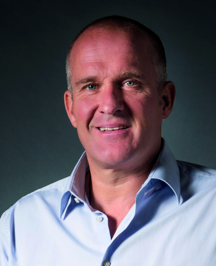 Ein Portraitfoto von Martin Braxenthaler. Er lächelt freundlich in die Kamera. Der Hintergrund ist grau. Er trägt ein blaues Hemd.